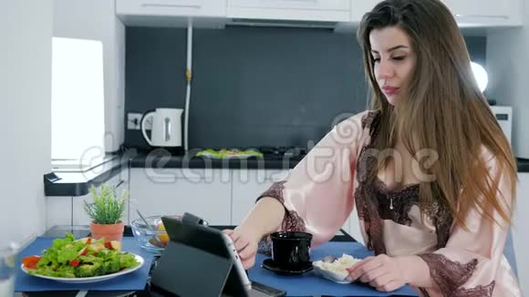 穿着睡衣的厨房女孩坐着平板电脑看着桌子桌上放着豆腐在家喝茶视频的预览图