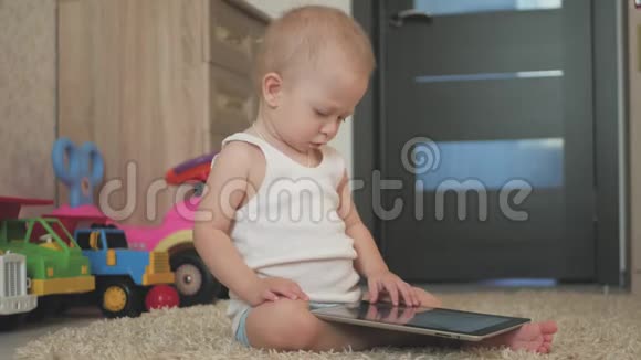 带着平板电脑的小男孩坐在家里的地板上在室内幼儿帅哥玩屏幕视频的预览图