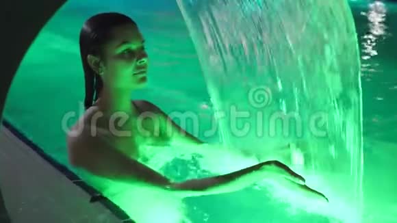 夏季晚上女性可以在度假胜地的清爽瀑布中畅游游泳池视频的预览图
