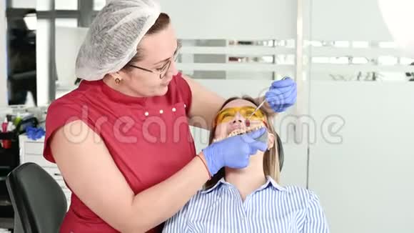 那个戴着黄色防护眼镜的漂亮金发女孩检查了她张开的嘴女性牙医检查视频的预览图