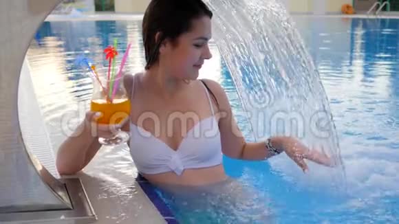 泳池瀑布下双手捧鸡尾酒的女性肖像视频的预览图