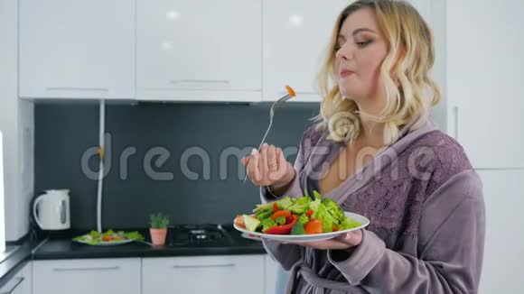 年轻女性穿着长袍在厨房吃健康食品喝着玻璃水视频的预览图