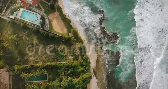 空中无人机飞越拍摄田园诗般的海洋海岸线起泡的白色波浪到达异国情调的热带度假胜地海岸房屋视频的预览图