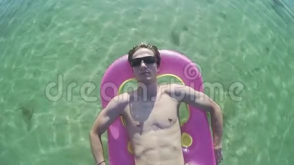 在热带海滩上的海上充气床垫上年轻游客戴着太阳镜放松慢动作视频的预览图