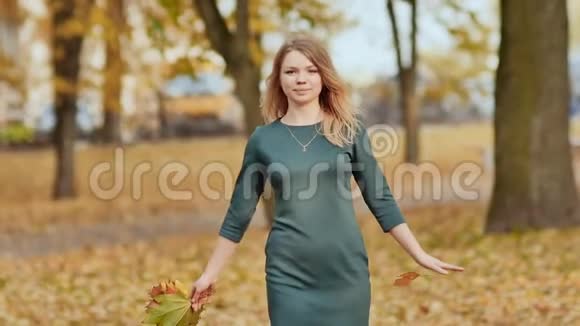 迷人的年轻女孩在相机上欢快地摆着姿势享受着秋天在五颜六色的树间旋转美丽美丽视频的预览图