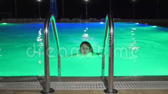 身材匀称的女性游泳进入有彩色照明的晚间游泳池视频的预览图
