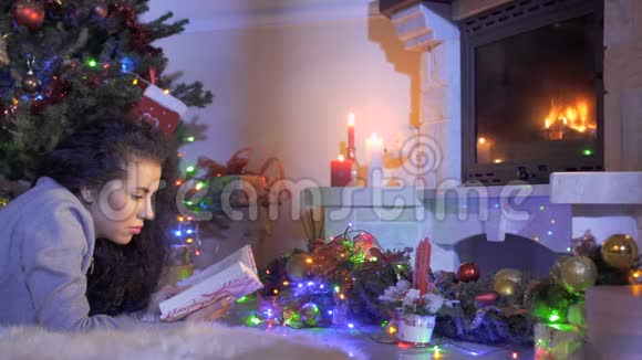 漂亮的黑发女人在圣诞树和壁炉附近看书视频的预览图