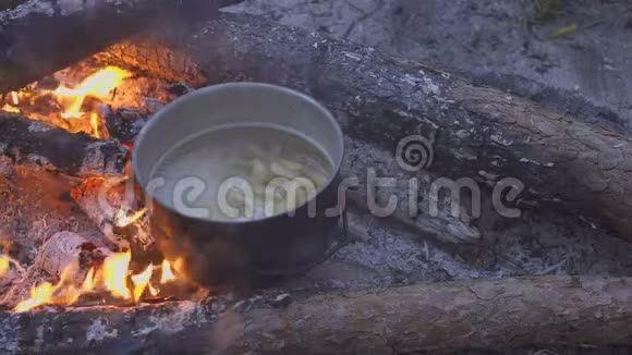 在晚林的篝火上用大锅煮意大利面厨师用勺子搅动食物特写视频的预览图