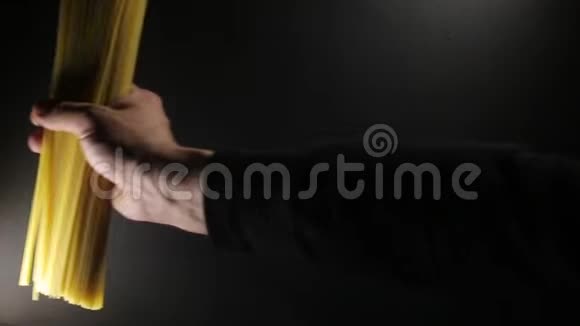男人把金色的生面条放在深黑的背景上视频的预览图