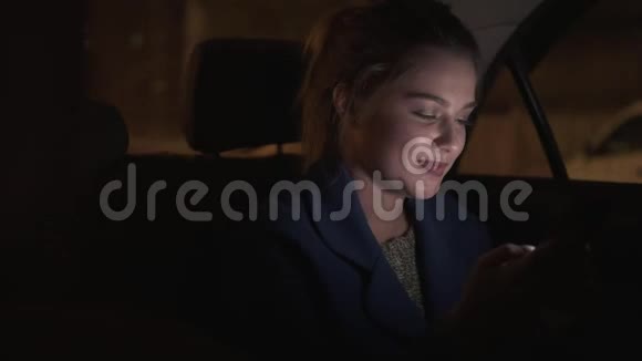 快乐的微笑女孩晚上坐出租车坐在后座上用她的智能手机发短信快乐的女人视频的预览图