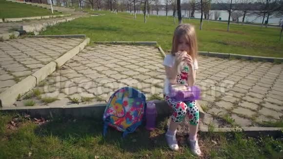 金发小女孩在晴天在公园吃午饭视频的预览图