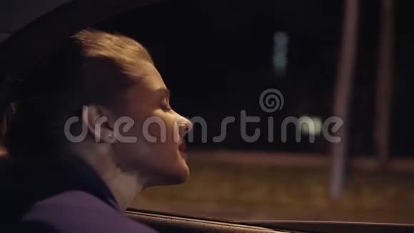 从车上看美丽的年轻女子从车窗里探出头来晚上看着城市慢动作视频的预览图