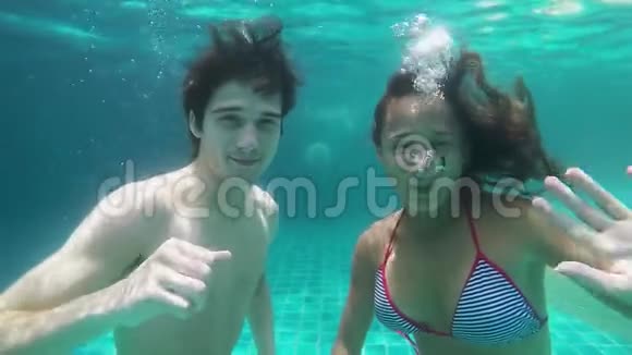 年轻的幸福夫妇在游泳池的蓝水里放松手对着镜头挥舞动作缓慢高清1920x1080视频的预览图