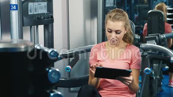 有魅力的年轻女性在健身俱乐部使用平板电脑视频的预览图
