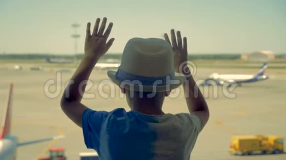一个戴帽子的男孩透过机场的窗户看飞机视频的预览图