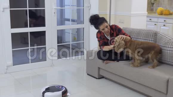 年轻的女人抚摸她的狗因为他害怕真空清洁机器人视频的预览图