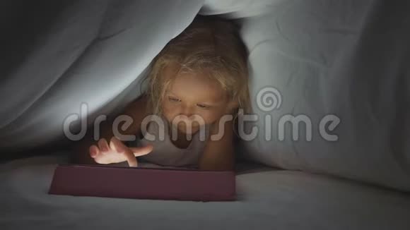 小可爱的女孩躺在羽绒被下睡觉时使用数字平板设备视频的预览图