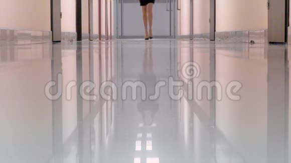 穿着黑色连衣裙和高跟鞋走在办公楼走廊上的年轻女子视频的预览图