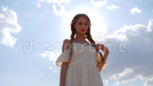 蓝色天空背景下白色连衣裙带辫子的可爱女性背光视频的预览图
