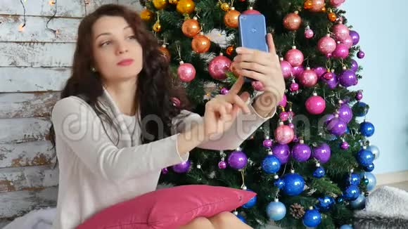 圣诞节概念年轻女子在装饰圣诞树附近自拍照片视频的预览图