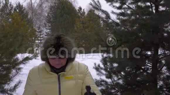 在冬季针叶林中享受新鲜空气的成熟女人女人走路北欧人用杆子走路视频的预览图