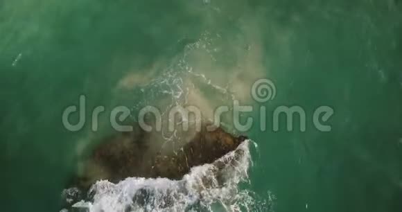 空中无人机拍摄的美丽的绿色海浪拍打海岸附近的一块珊瑚礁石头创造了美丽的白色泡沫视频的预览图