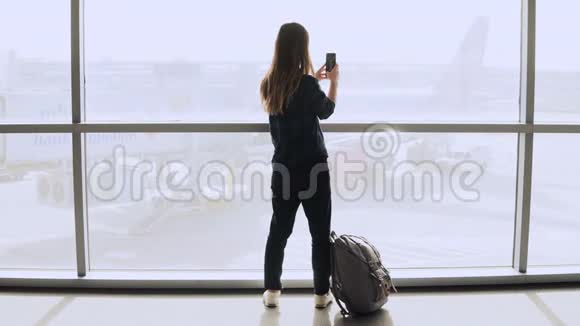 女孩在机场窗口附近自拍走开快乐白人女性游客使用智能手机在终点站大厅4K视频的预览图
