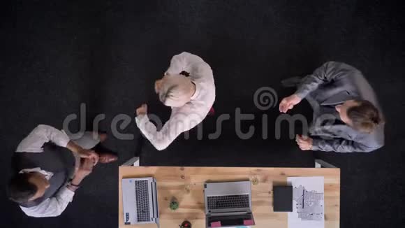 三个穆蒂族的工人正在桌子旁跳舞手提电脑和眼镜办公室里有香槟公司聚会视频的预览图