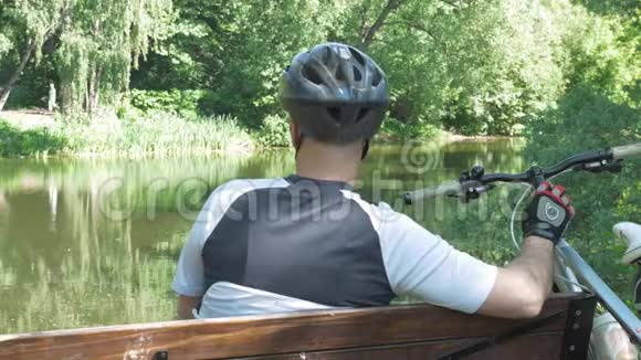 一个骑自行车的人夏天在公园里休息他坐在池塘附近的长凳上视频的预览图