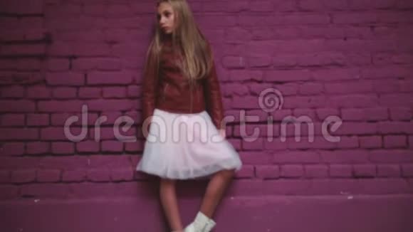 穿皮夹克和裙子的女孩靠近砖墙视频的预览图
