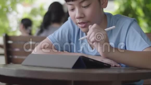 可爱的亚洲男孩使用平板电脑年轻的十几岁男孩在数字平板电脑上做作业默默面对视频的预览图