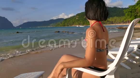 美丽的亚洲女人坐在美丽的海滩上的躺椅上视频的预览图