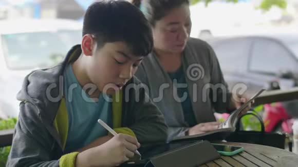 亚洲男孩玩平板电脑和他的母亲交谈微笑着面对视频的预览图