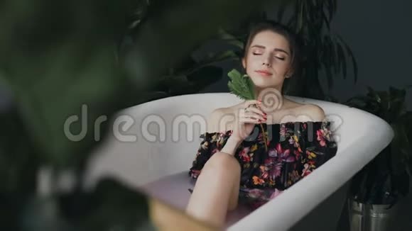 年轻女子在水疗中心的热水浴中放松美丽的女孩沐浴着芬芳的花朵眼睛放松视频的预览图