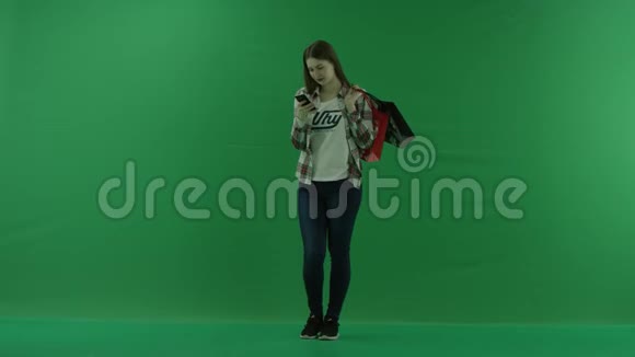 女孩站在半个转弯处看着左边肩膀上放着袋子在绿色手机的帮助下聊天视频的预览图