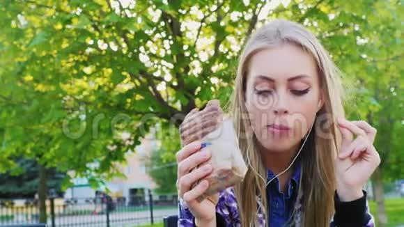 迷人的女人在公园里吃三明治听音乐视频的预览图