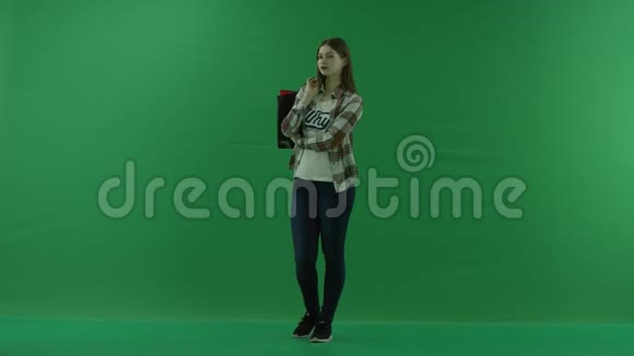 女孩站在一个半转弯处向左看肩膀上放着包裹在绿色的屏幕上等待一些东西视频的预览图
