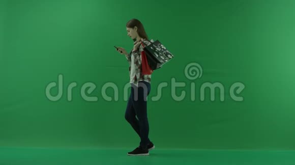 女孩站在左边肩膀上放着袋子在绿色屏幕上借助手机聊天视频的预览图