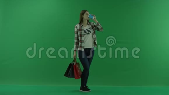 女孩站在半个转弯处看着右边手里拿着袋子在绿色的屏幕上喝着杯子里的东西视频的预览图
