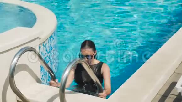 穿着泳衣的女孩爬上了水中游泳池边缘的楼梯视频的预览图