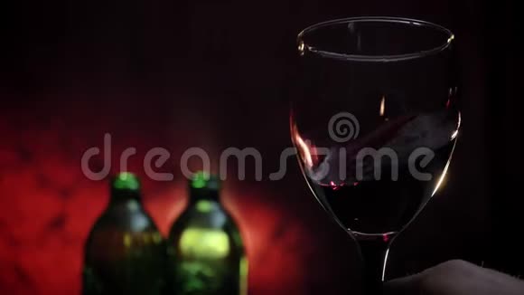 男人的手拿着一杯慢腾腾的红酒两瓶深红色的背景视频的预览图