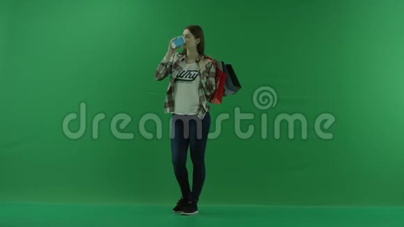 女孩站在半个转弯处看着左边肩膀上放着袋子喝着绿色杯子里的东西视频的预览图