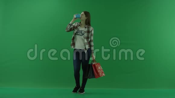 女孩站在半个转弯处看着左边手里拿着袋子在绿色的屏幕上喝着杯子里的东西视频的预览图