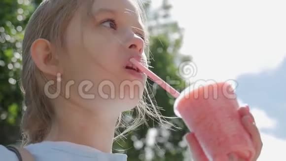 可爱的小女孩正在用吸管喝鸡尾酒在阳光明媚的天气里站在公园里视频的预览图