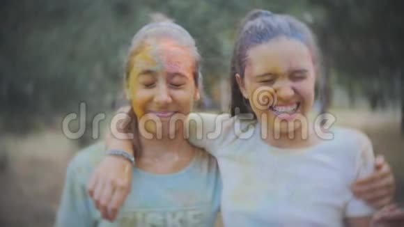 两个十几岁的女孩涂抹了彩色粉末霍利在夏季公园里慢动作地洒水视频的预览图