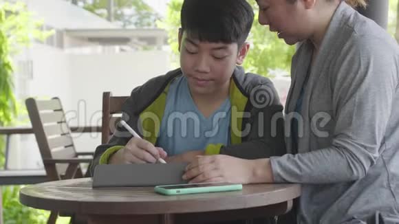 亚洲男孩玩平板电脑和他的母亲交谈微笑着面对视频的预览图