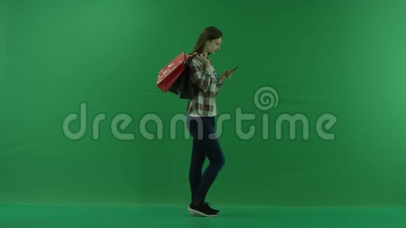 女孩站在她的右边肩膀上放着袋子在绿色屏幕上借助手机聊天视频的预览图