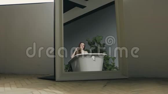 坐在摄像机旁边一个留着长发的漂亮女孩在一个充满热水的白色浴缸里放松一头长发的年轻女子视频的预览图