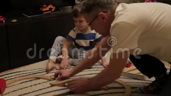 祖父和他的孙子在地板上的一条木制铁路里玩耍一个跟爷爷在一起三年的小男孩视频的预览图