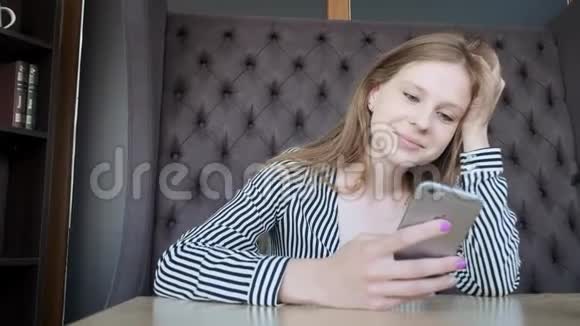 年轻漂亮的女孩在时尚咖啡馆使用智能手机使用应用程序在窗户对面视频的预览图